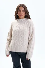 Buzo de punto en color beige con diseño de trenzas, cuello alto con capucha integrada, manga larga y puños acanalados.