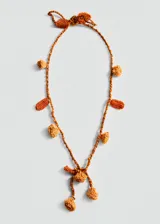 Collar largo de estilo artesanal confeccionado en tejido crochet color naranja y beige. Presenta un diseño con flores tejidas, abalorios decorativos y cierre mediante nudo ajustable.