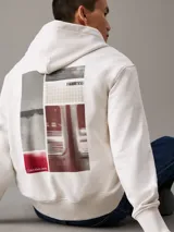 Buzo con capucha confeccionado en felpa de algodón regenerativo color blanco. Tiene corte relaxed, capucha con cordón, puños y bajo de canalé, logo bordado en el bajo en el mismo tono y estampado fotográfico digital de Calvin Klein en la parte trasera.
