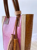 Bolso matero de cuero color fucsia y marrón con textura croco, doble asa de mano marrón y detalle de borlas de cuero marrón.
