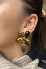 Caravanas con diseño floral compuestas por pétalos de piedras naturales en tonos violeta y lila, con un centro de piedra clara y un dije colgante en forma de gota de color amatista, engarzadas en metal dorado.