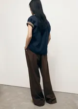 Pantalón de vestir marrón de tiro bajo y diseño wide leg, con pinzas frontales, trabillas para cinturón, bolsillos laterales y cierre oculto con botón, gancho y cremallera.