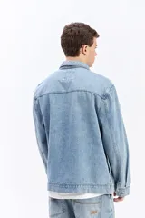 Campera de jean de corte recto y lavado desgastado, con cuello clásico, cierre frontal con botones metálicos y un bolsillo grande aplicado en el pecho.