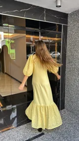 Vestido largo color amarillo pálido, con escote en V, mangas cortas abullonadas con detalle de calado y ruedo con volantes y calado.
