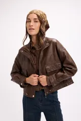 Campera corta de cuero sintético en color beige, con diseño de calce relajado, cierre frontal metálico, bolsillos con solapa en el frente y cordón ajustable en el ruedo.