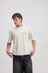 Remera boxy de algodón color beige, de silueta amplia y corta, con mangas cortas y pequeño estampado en el pecho.