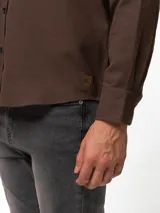 Camisa de franela color azul marino, de manga larga, con cuello abotonado, un bolsillo frontal y cierre de botones.