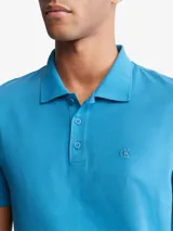 Chomba celeste de manga corta, confeccionada en mezcla de algodón y poliéster. Presenta cuello clásico con solapa de dos botones y logo de Calvin Klein bordado en el pecho.