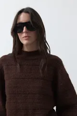 Sweater de punto color marrón chocolate, con cuello redondo, mangas largas abullonadas y puños ajustados. Presenta un diseño de textura acanalada horizontal y silueta relajada.