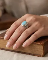 Anillo de plata envejecida con piedra natural ovalada de ópalo en tono celeste y detalles grabados en la banda.