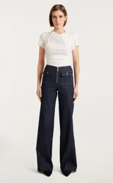 Pantalón acampanado de jean azul oscuro con bolsillos frontales con solapa y cierre frontal con cremallera metálica visible.