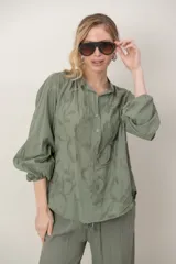 Camisa de algodón color verde militar con bordados florales al tono, cuello mao, cierre frontal parcial con botones y mangas abullonadas tres cuartos con puños elásticos.