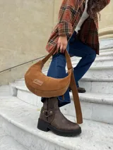 Cartera tipo hobo de cuero gamuzado color camel, con correa ajustable y etiqueta de cuero con logo grabado en el frente.