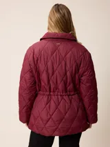 Campera acolchada de diseño matelassé con patrón de rombos, color bordó. Presenta cuello camisero, cierre frontal con cremallera metálica, cintura entallada con elástico y bolsillos laterales. Incluye un pequeño bordado distintivo en el pecho.