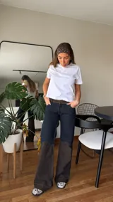 Pantalón de jean de tiro medio con diseño bicolor, combinando un tono azul oscuro en la parte superior y un tono marrón oscuro en la parte inferior. Presenta un corte recto y holgado.