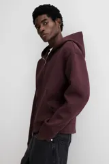 Campera con capucha en tejido efecto neopreno, color borgoña oscuro, con cierre frontal plateado y bolsillos canguro delanteros. Presenta un corte holgado y hombros caídos.