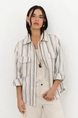 Chaqueta de algodón a rayas verticales en tonos beige y gris, con cuello camisero, cierre frontal con botones y mangas largas con puños abotonados. Tiene bolsillos delanteros con solapa y galones ondeados a tono.
