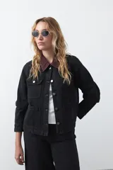 Campera de jean color negro con cuello de pana en tono marrón, cierre frontal con botones metálicos y bolsillos frontales tipo cargo.