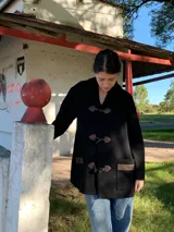 Saco negro de lana con cierre de broches tipo duffle coat, bolsillos laterales con solapa de cuero y detalle de trenza en la espalda.