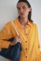Bolso de hombro tipo saco confeccionado en piel azul marino, con detalle de pespuntes blancos verticales, asas finas de hombro en color blanco y cierre fruncido.