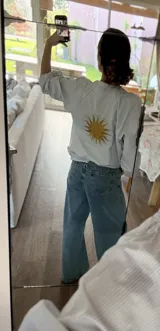 Camisa de corte suelto con estampado de rayas finas, cuello redondo y mangas largas con puños elásticos. Presenta un bordado central en la espalda con diseño de sol en color amarillo.