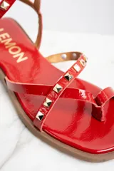 Sandalias rojas de charol con tiras finas, puntera cuadrada y cierre con hebilla al tobillo. Decoradas con tachas piramidales doradas.