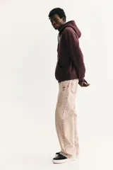 Canguro de corte holgado en color bordó, con capucha ajustable mediante cordones, hombros caídos y bolsillo frontal tipo canguro. Presenta un pequeño estampado central de un jarrón con flores coloridas.