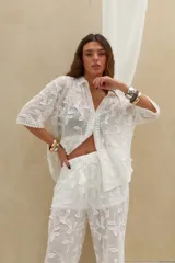 Camisa blanca de manga corta con diseño bordado de hojas y flores, cuello camisero y cierre frontal de botones.