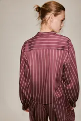 Camisa de cuello subido y manga larga con puños anchos, confeccionada en tejido satinado con diseño de rayas verticales.
