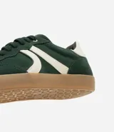 Championes de mujer estilo chuteira, color verde oscuro con detalles en blanco y suela de goma color caramelo. Presentan un diseño de corte bajo con cordones y un logo lateral en forma de arco.