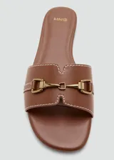 Sandalias planas de color marrón, con tira ancha en el empeine decorada con costuras blancas y un detalle metálico dorado. Diseño destalonado y puntera redondeada.