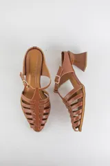 Sandalias de cuero color beige estilo cangrejera con punta fina, diseño de tiras entrelazadas, tira ajustable en el tobillo con hebilla dorada y taco geométrico de madera.
