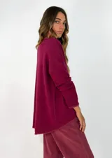 Sweater de punto gris con cuello redondo, mangas largas y diseño asimétrico, siendo más corto en la parte delantera y más largo en la trasera, con detalles de terminación en contraste.