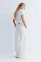 Pantalón de jogging de corte ancho y tiro alto, color gris melange, confeccionado en tejido de felpa con interior cepillado suave. Posee cintura elástica fruncida con cordón de ajuste oculto, bolsillos laterales y un bolsillo trasero abierto.