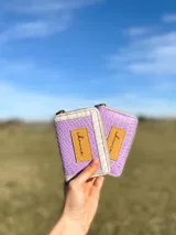 Billetera pequeña con cierre metálico, cuerpo principal de cuero lila texturizado y ribetes en color crema. Presenta un parche de cuero marrón con la palabra "chowie" escrita en cursiva.