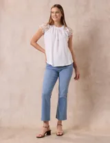 Blusa negra de crepe con apliques de crochet en los hombros. Tiene cuello redondo, mangas cortas y espalda con abertura ojal y botones.