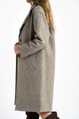 Tapado largo de corte oversize en color beige, con solapas clásicas y cierre frontal con botones. Presenta un diseño minimalista y elegante, ideal para un look sofisticado.