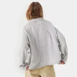 Sweater de punto gris con cuello polo y cierre frontal parcial. Presenta un diseño oversize y logo bordado en el frente.