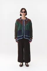 Cardigan de punto con diseño multicolor en tonos marrones, bordó y detalles en amarillo y celeste. Presenta cuello tipo polo, cierre frontal con botones, bolsillos aplicados en el frente y mangas con trama trenzada y coderas bordadas.