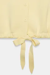 Chaqueta de punto color amarillo claro, con cuello solapa, manga corta abullonada, cierre frontal con botones y bajo ajustable con lazo.