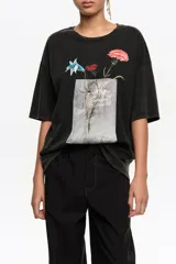 Remera negra de corte recto y holgado, confeccionada en algodón orgánico. Presenta cuello redondo, mangas cortas y estampa frontal de un ramo de flores en tonos coloridos con detalles artísticos.