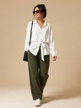 Camisa de seda con cuello camisero, manga larga con presilla para arremangar, cierre frontal con botones y lazo ajustable en la cintura que genera un efecto fruncido.