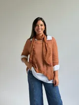 Sweater de punto color naranja con diseño asimétrico, que incluye una bufanda a juego con detalles bordados y una camisa blanca de base integrada.