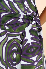 Pareo largo de diseño envolvente con nudo lateral, confeccionado en tejido fresco con estampado de motivos orgánicos en tonos verde y violeta sobre fondo blanco.