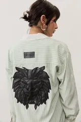 Camisa oversize a rayas color verde menta con cuello y puños en contraste de color blanco. Presenta cierre frontal con botones y un bolsillo aplicado en el pecho.