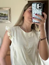 Blusa de lino color marfil, sin mangas, con detalles de volados en los hombros y cuello redondo.