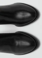 Bota de caña alta confeccionada en piel bovina, con diseño de punta fina y tacón de bloque. Presenta un acabado liso y cierre lateral.