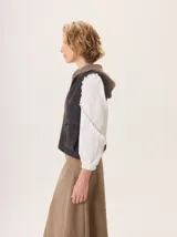 Chaleco de punto con capucha, confeccionado en lana. Presenta un diseño bicolor con cuerpo en tono beige de textura acanalada y capucha en tono marrón. Incluye una etiqueta de cuero en la parte posterior.