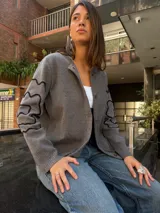 Cárdigan gris de algodón, con cuello redondo, botones frontales y mangas largas con diseño de líneas onduladas en negro.