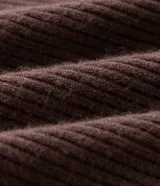Cardigan de punto color beige, con diseño alargado y puntas asimétricas. Presenta mangas largas, cuello tipo chal y recortes canelados que aportan textura y movimiento a la prenda.